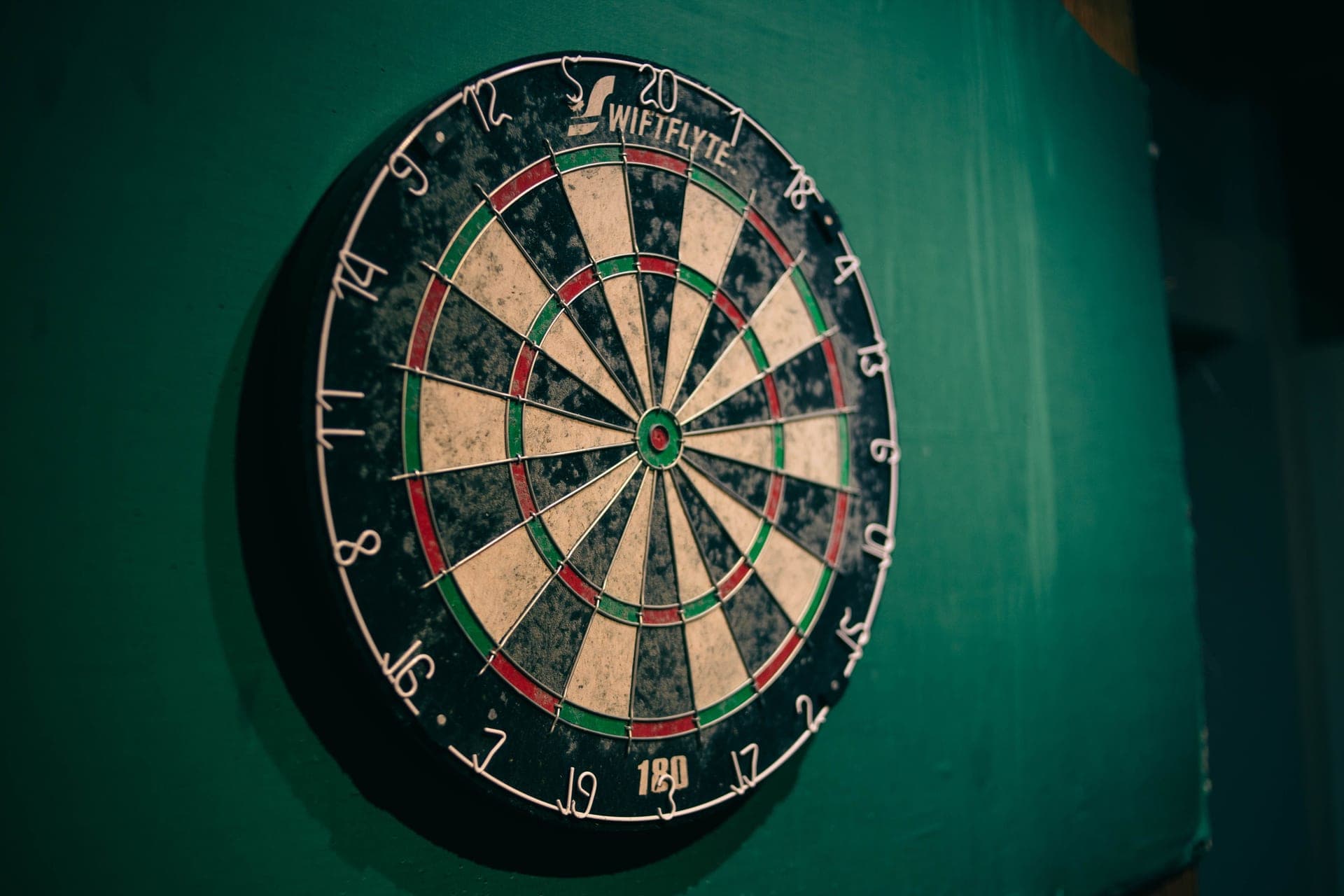 A bristle dartboard mounted on a wall with darts in the treble bed
