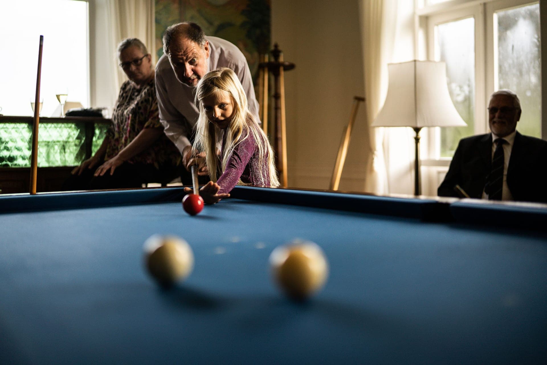 A grandfather teaching a young girl to play pool on a home table